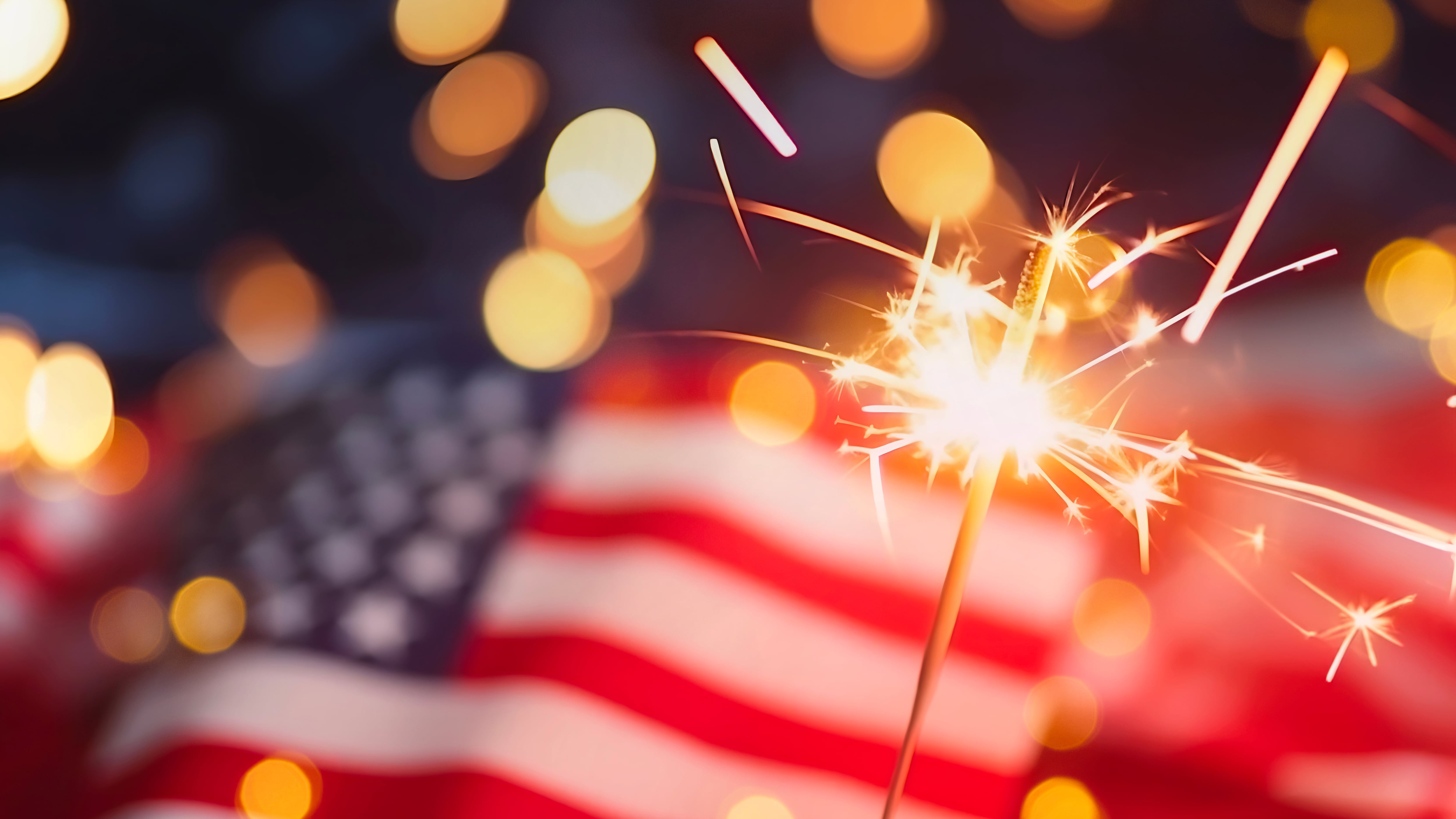 Sparkles with lights in soft focus and the American flag in the background.